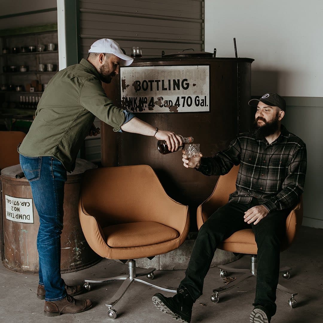 A guide pours bourbon for a guest beside an old bottling tank sign